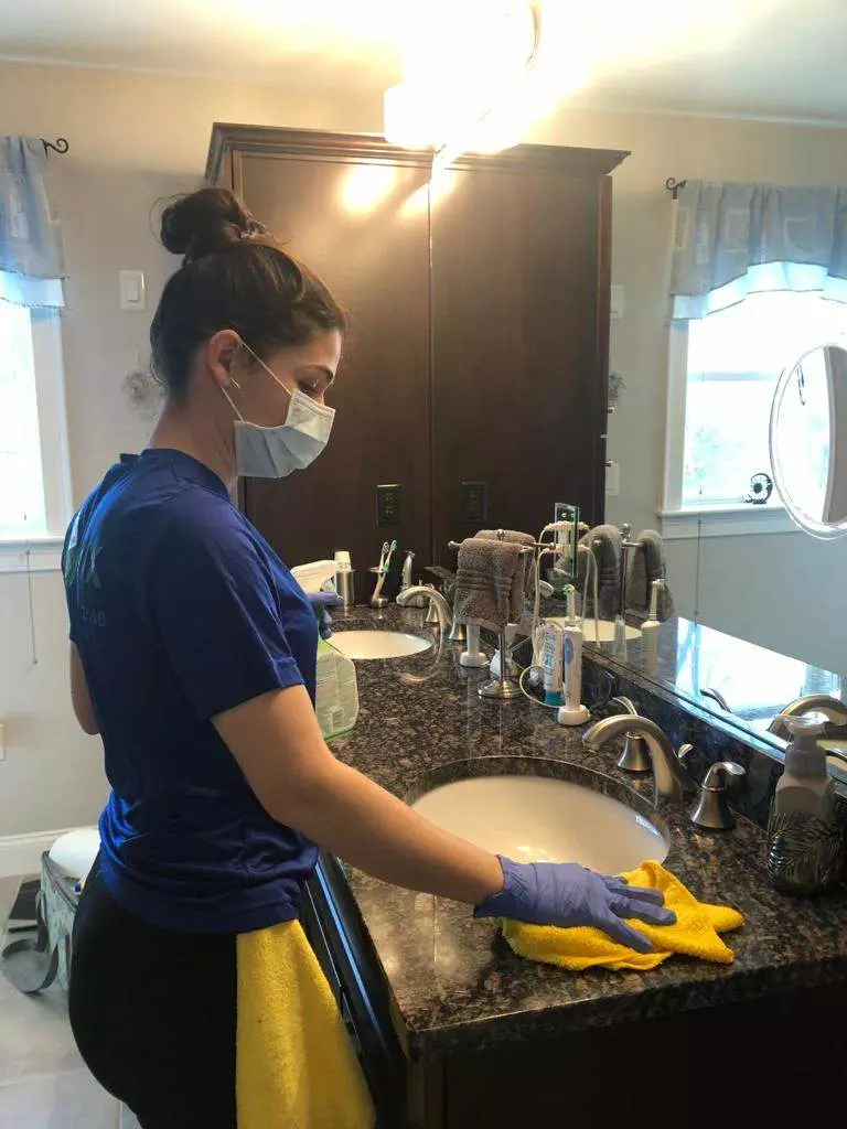 A woman wearing gloves cleaning a bathroom.