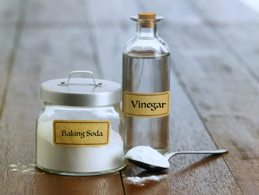 an image of a glass containers with baking soda and vinegar inside, accompanied by a spoonful of baking soda placed next to it