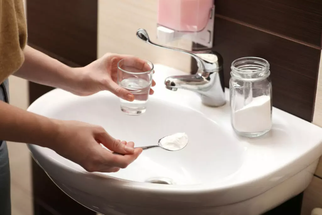 hands of a woman pouring vinegar and baking soda into the kitchen sink