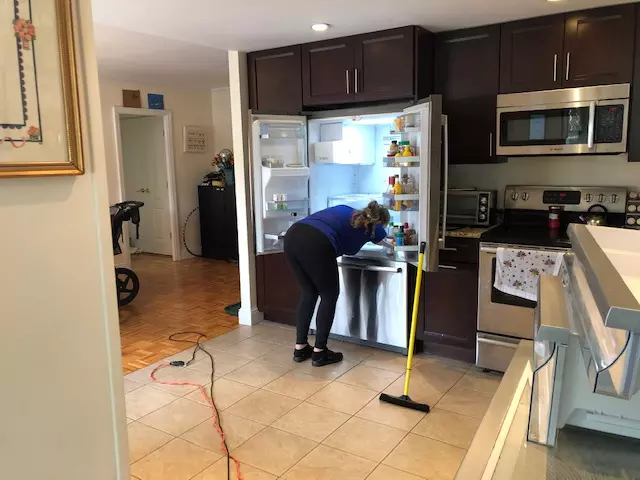 A woman cleaning a kitchen in Boston with a broom for a Cleaning Company.