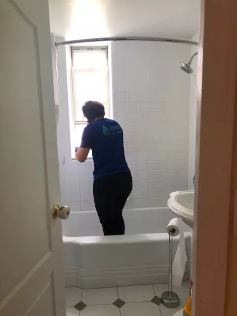 an image of a female onix cleaner scrubbing the bath tub area