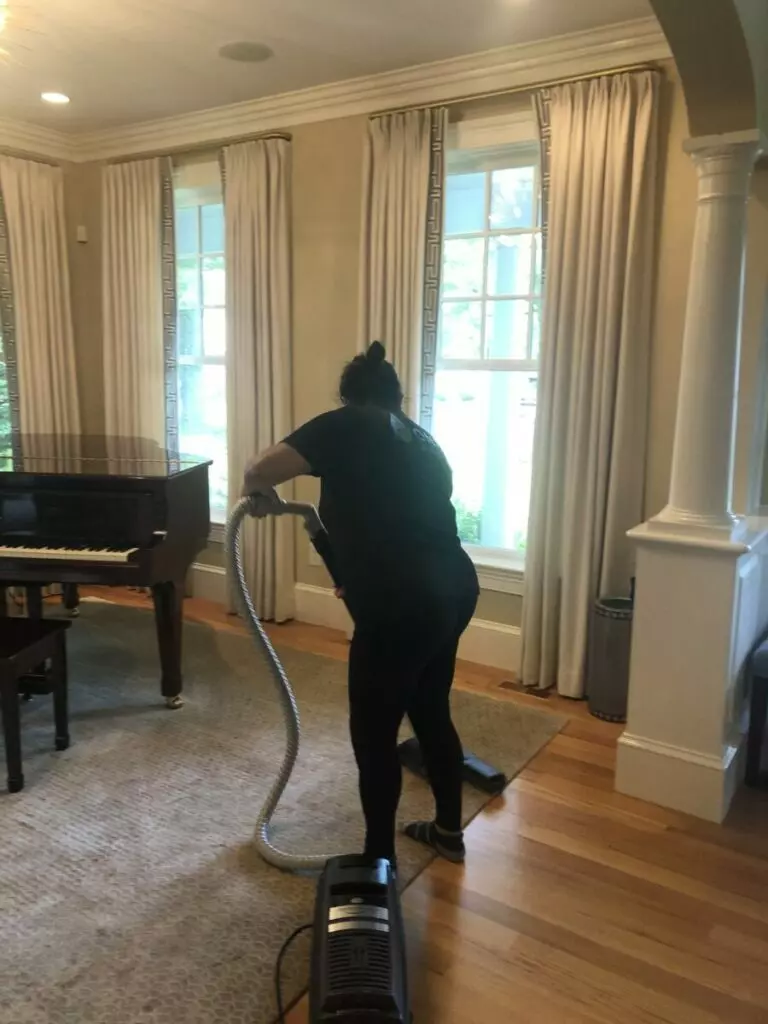 A woman from a cleaning company in Boston diligently vacuuming in a living room with a piano.