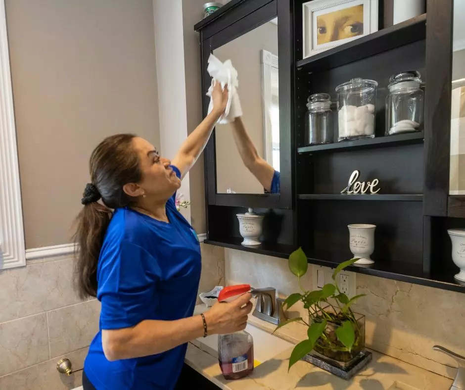 A woman meticulously cleaning her bathroom mirror.