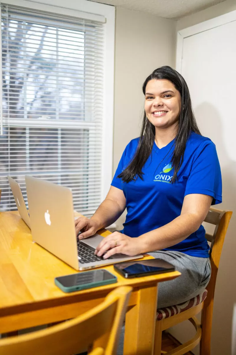 A woman in a blue shirt sitting at a table with a laptop, using templates for bathroom cleaning.