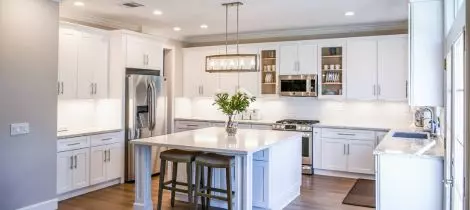 A kitchen with white cabinets and a center island is in need of a deep cleaning.