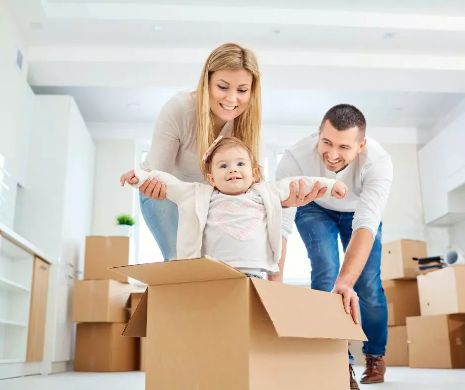 A family settling into their new home with a baby playfully sitting in a cardboard box, after a thorough move in and move out cleaning service in Boston.