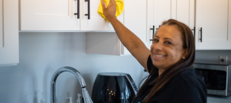 A woman cleaning an apartment kitchen with a yellow mop.