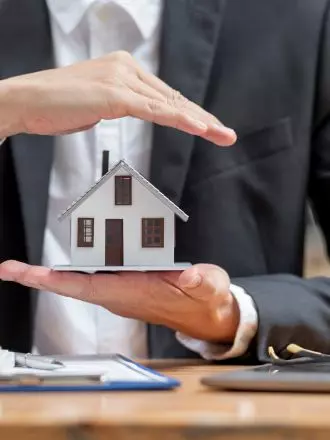 Protection of a miniature house by two individuals' hands, symbolizing insurance or security in real estate and cleanliness ensured through house cleaning templates.