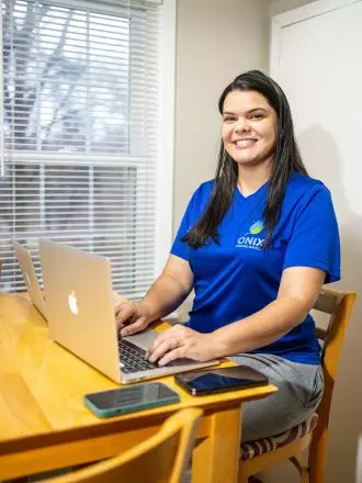 Woman working on a laptop at a home office setup in her bedroom, amidst her ongoing bedroom cleaning process.