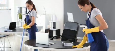 Two women using a standard cleaning checklist to clean a desk in an office.