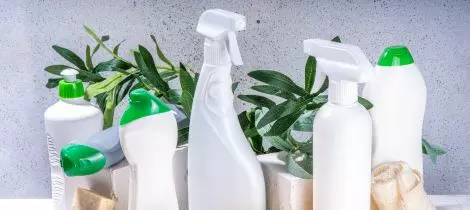 Assorted green cleaning supplies and green plants on a speckled background.