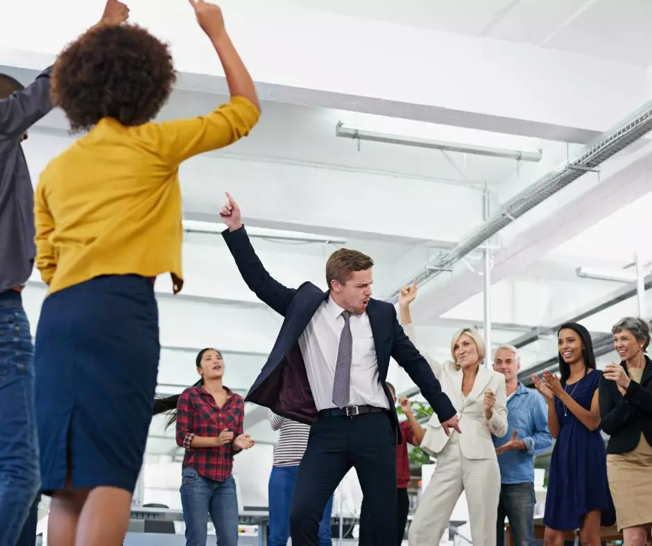 Colleagues celebrating in the office with one person dancing enthusiastically, amidst commercial cleaning templates displayed around.