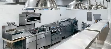 A clean and empty commercial kitchen with stainless steel appliances and work surfaces, complete with kitchen cleaning templates for maintenance.