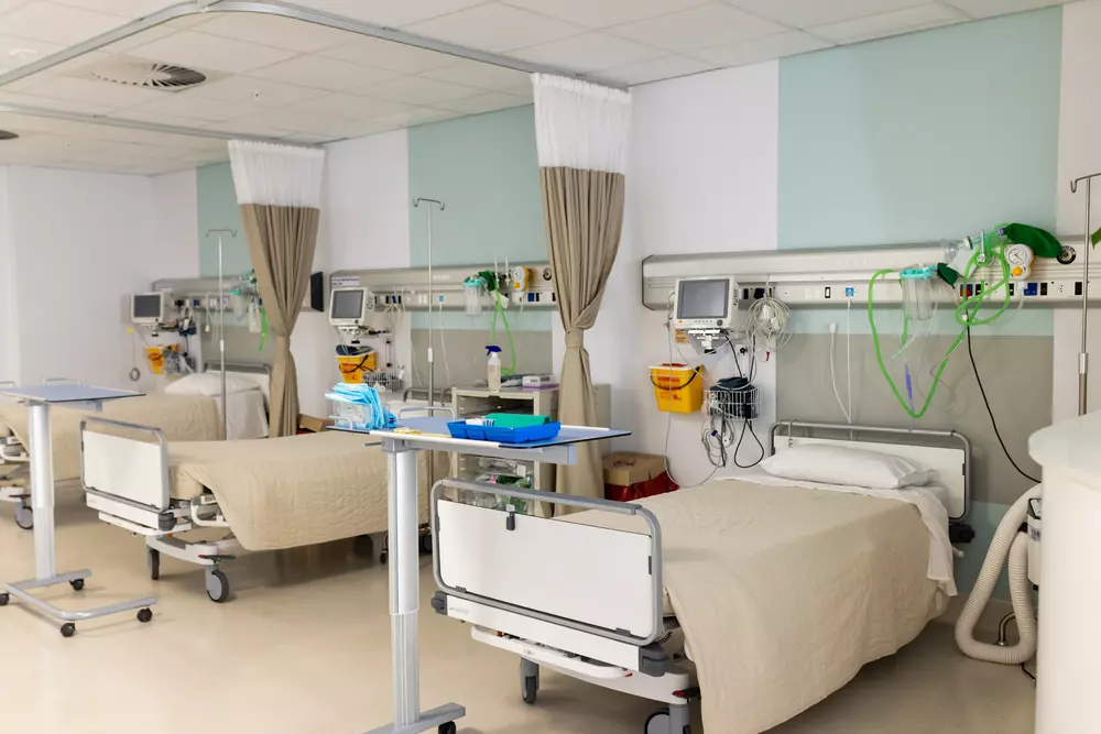 A hospital room with three empty beds, medical equipment, monitors, and privacy curtains, ready to provide essential services to patients.