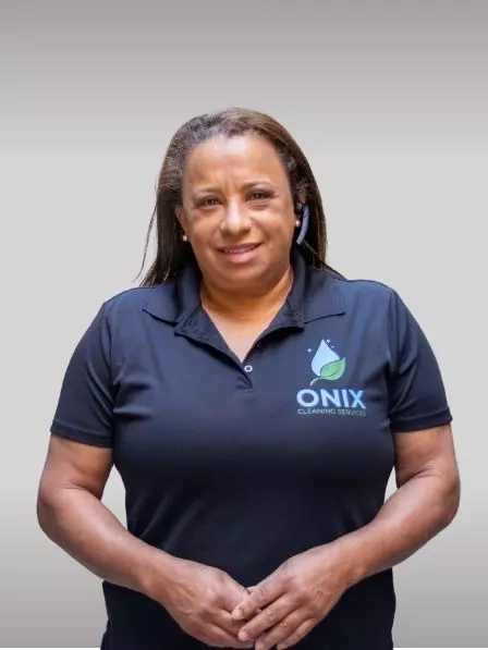 A person wearing a navy blue polo shirt with the "ONIX Cleaning Services" logo stands against a plain background, smiling slightly and holding their hands together, as if posing for a portrait in an art gallery.