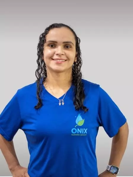 A person with long curly hair, wearing a blue Onix Cleaning Service t-shirt and a smartwatch, stands against a plain gallery background.