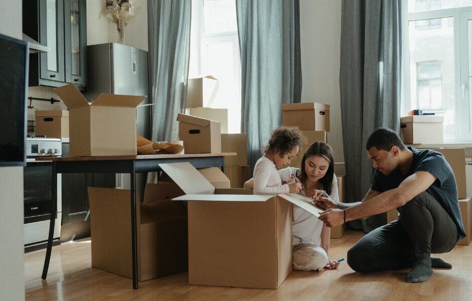 A family with a young child sits on the floor among cardboard boxes, unpacking and organizing belongings in a bright, spotless space after their Move-In Cleaning Boston service; Move-In/Move-Out Cleaning in Boston